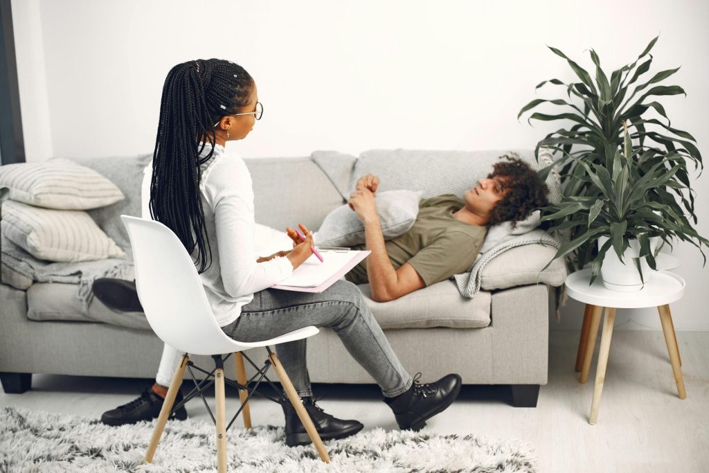 A therapist conducting a session with a patient lying on a sofa in a bright room.